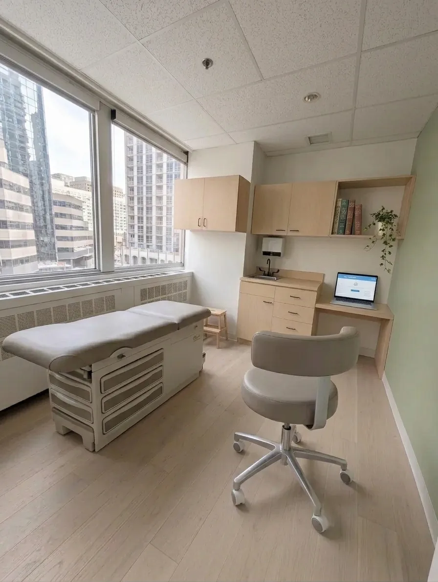 An exam room at Button Health, 790 Bay Street, with natural light, a white-oak floor, and a sage accent wall