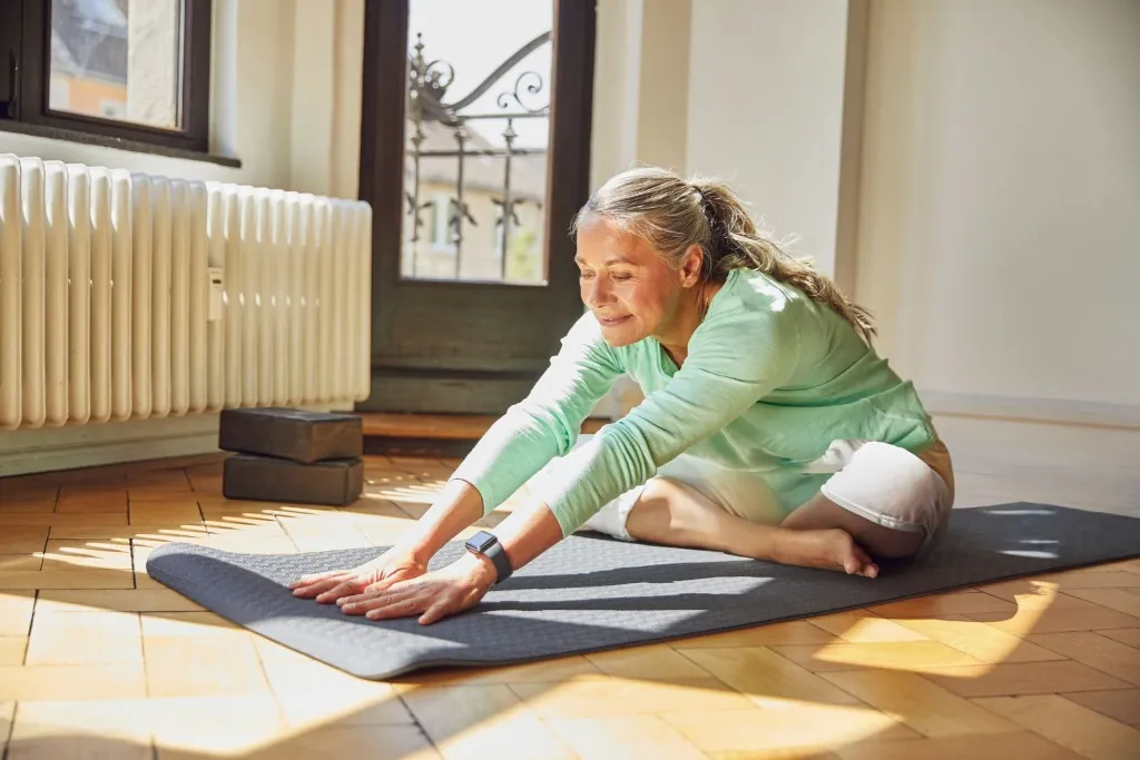 A woman stretching forward on an exercise mat in a sunlit room