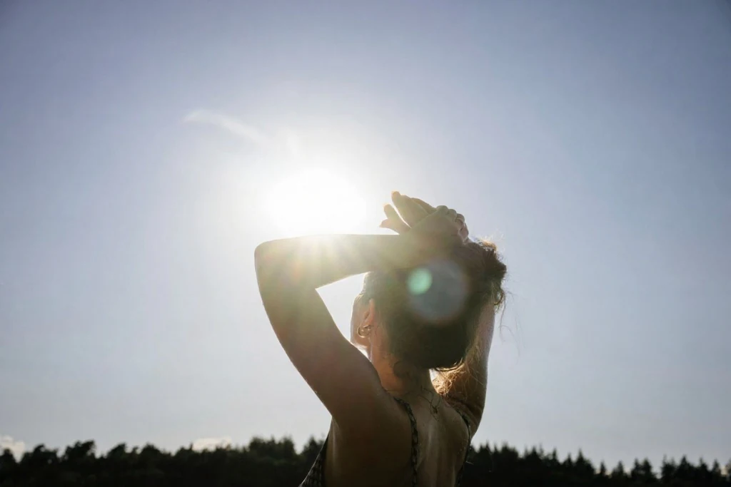 A person shielding their eyes from the bright midday summer sun under a clear blue sky