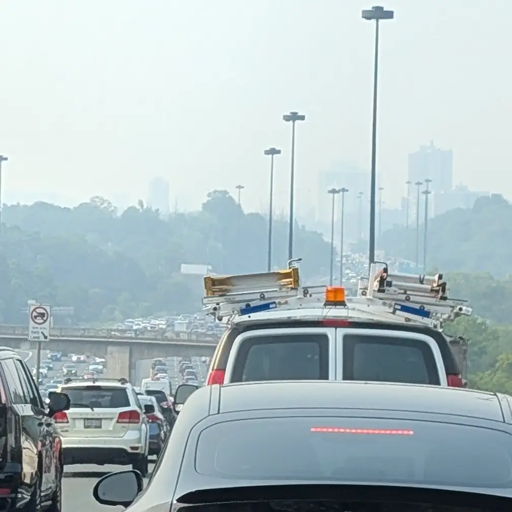 Bumper-to-bumper Toronto highway traffic under thick wildfire smoke, the skyline barely visible through the haze